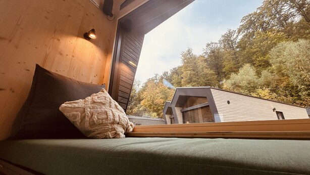 Una cabaña de madera con un asiento junto a la ventana que da a un área boscosa.