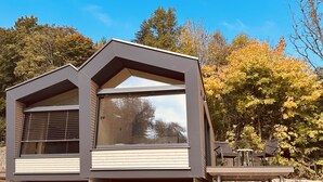 Una cabaña moderna con techo inclinado, ventanas amplias y una terraza con mobiliario exterior.