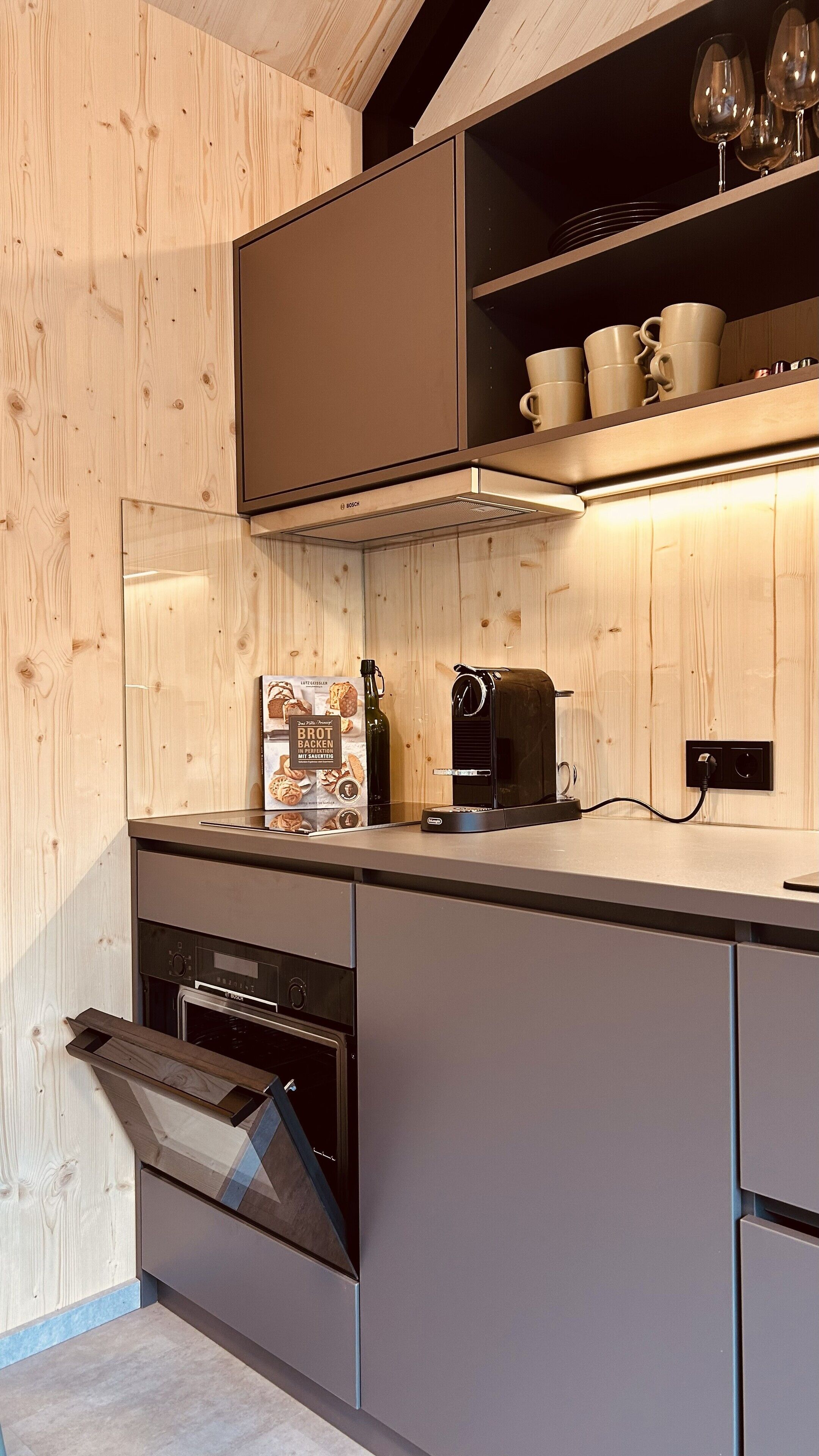 Eine moderne Küche mit Holzschnitzereien, einer Bosch-Dunstabzugshaube, einer Kaffeemaschine und einem Weinkühlschrank.