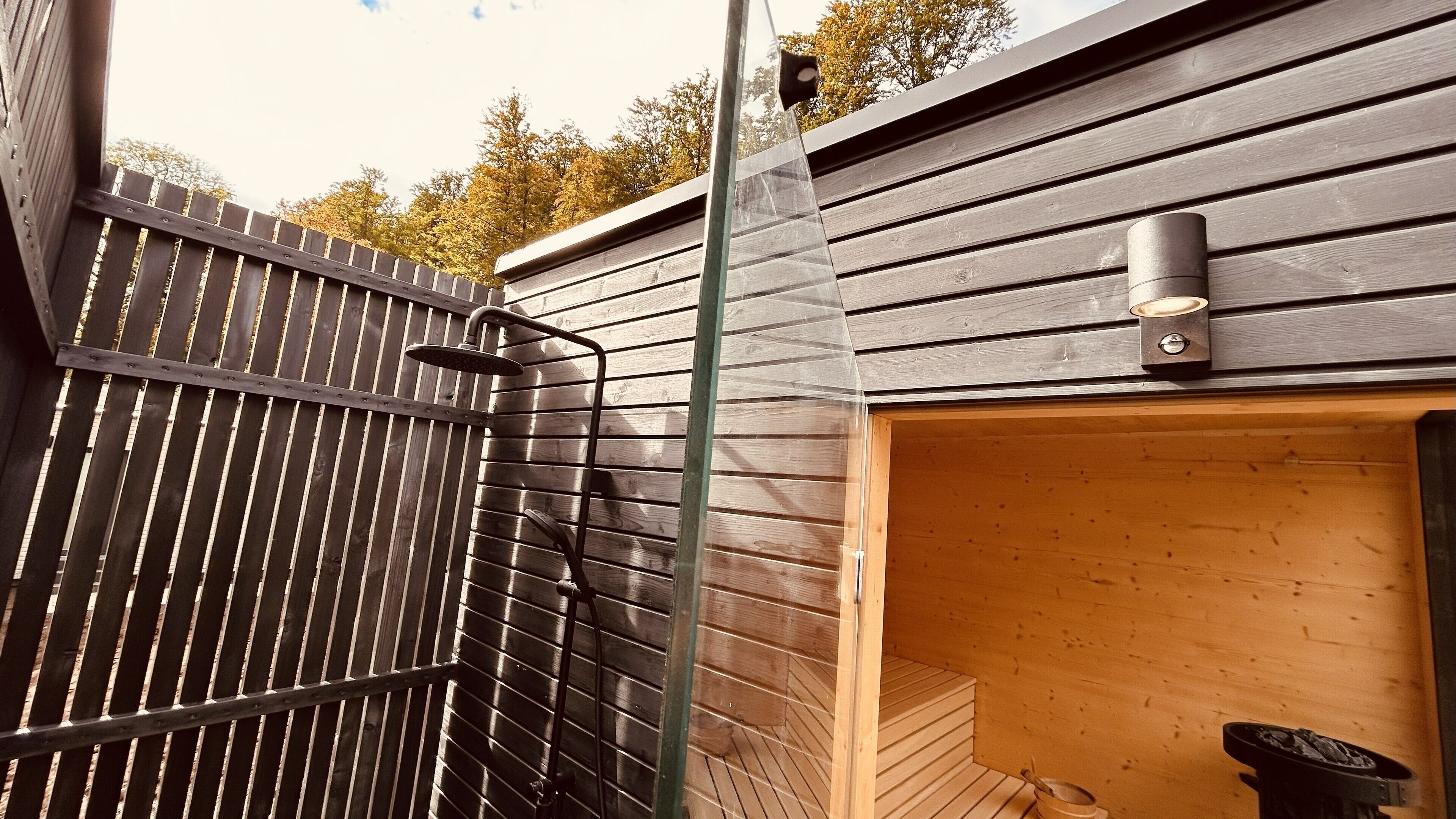 A modern outdoor shower with a metal frame and a wooden deck.