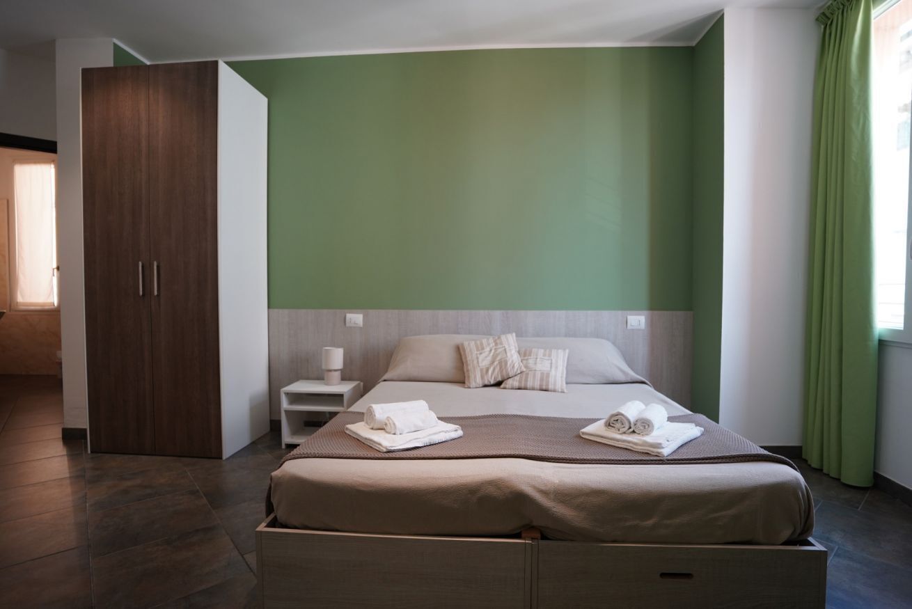 Een hotelkamer met een bed, nachtkastje, garderobe en raam met gordijnen.