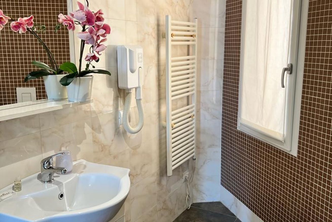 Une salle de bain avec un lavabo blanc, un miroir, un porte-serviettes et une orchidée en pot.