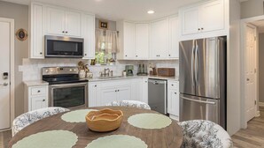 A modern kitchen with white cabinets, stainless steel appliances, and a round dining table with placemats. - La Casita- Trailside Retreat in Collegedale (Collegedale)