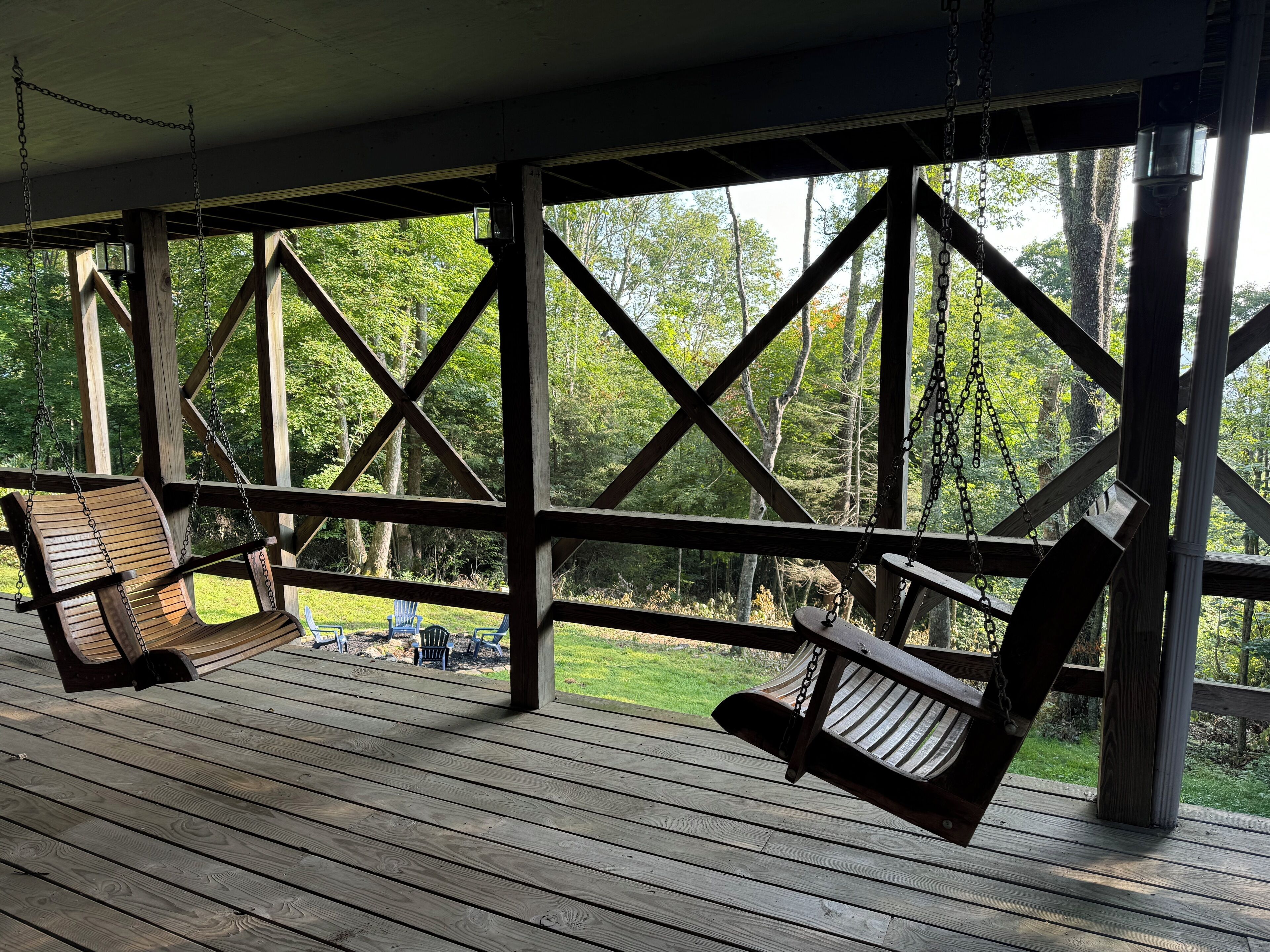 Een houten terras met twee schommelstoelen en uitzicht op een bos.