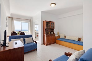 A living room with a blue sofa, wooden cabinet, and a view through a window.
