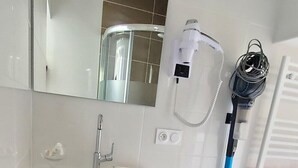 Une salle de bain avec un meuble-lavabo blanc, un miroir, un sèche-cheveux et un aspirateur.