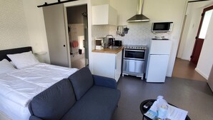 Une chambre à coucher avec un lit, un canapé gris et une kitchenette équipée d’un four à micro-ondes, d’une cuisinière et d’un réfrigérateur.