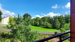 Une vue depuis un balcon donnant sur un champ verdoyant, un bâtiment et des arbres, le tout sous un ciel dégagé.