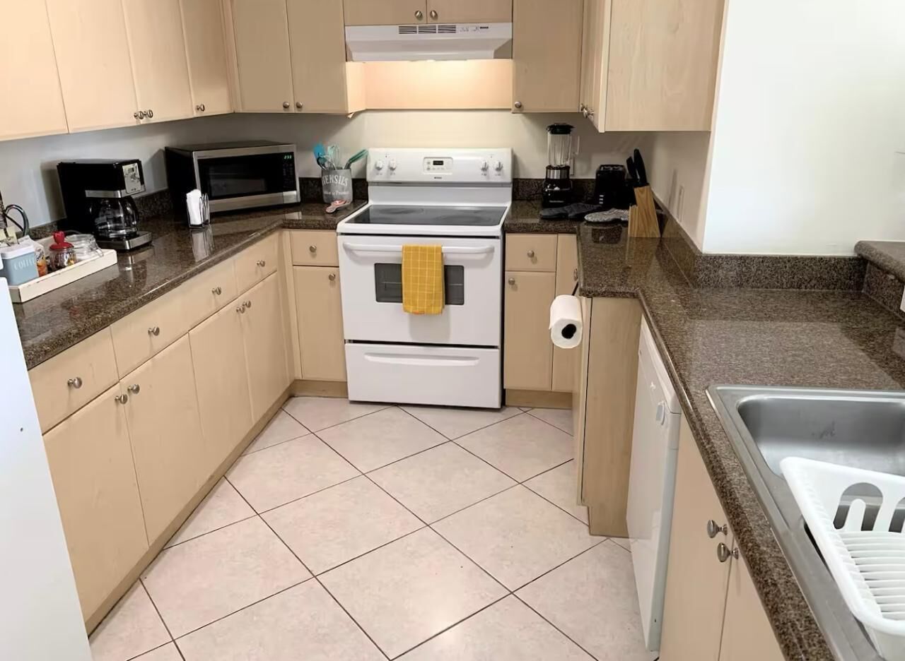 A kitchen with beige cabinets, a white stove, a microwave, and a sink.