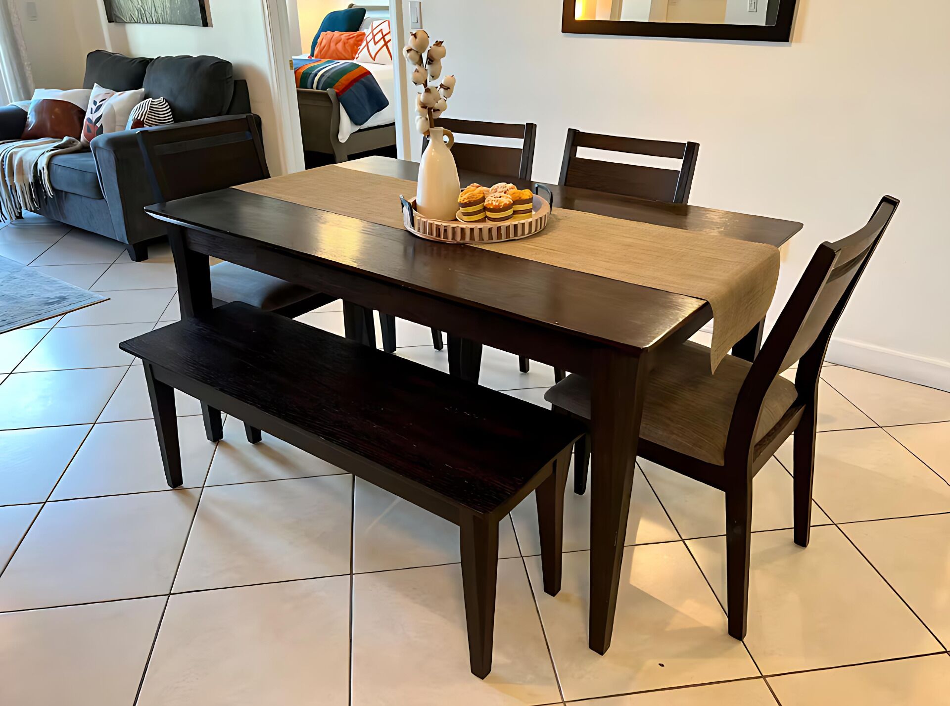 A dining area with a wooden table and benches, a vase with flowers, and a bowl of pastries.