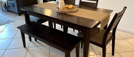A dining area with a wooden table and benches, a vase with flowers, and a bowl of pastries.