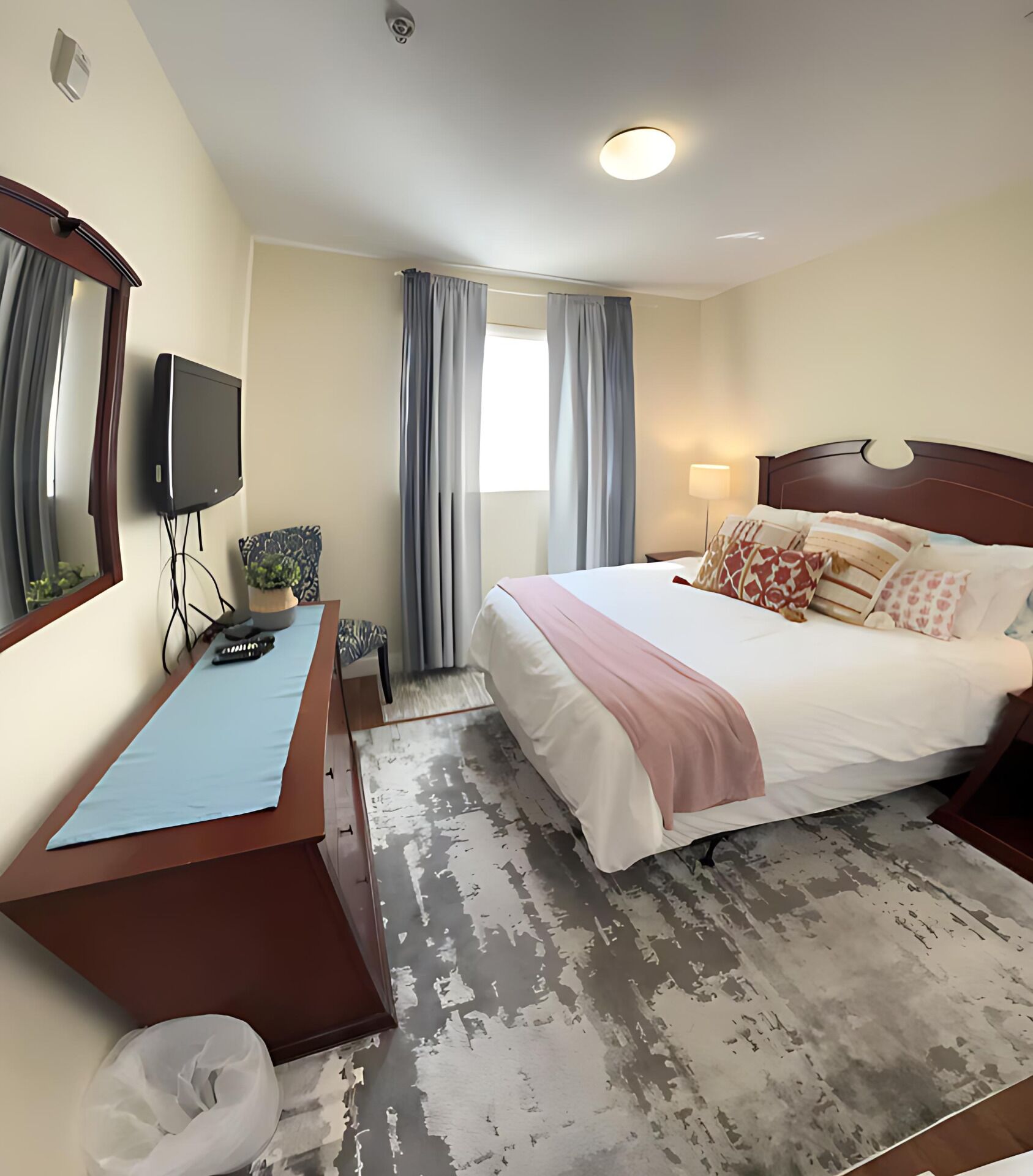 A hotel room with a bed, a desk, a television, and a window with curtains.