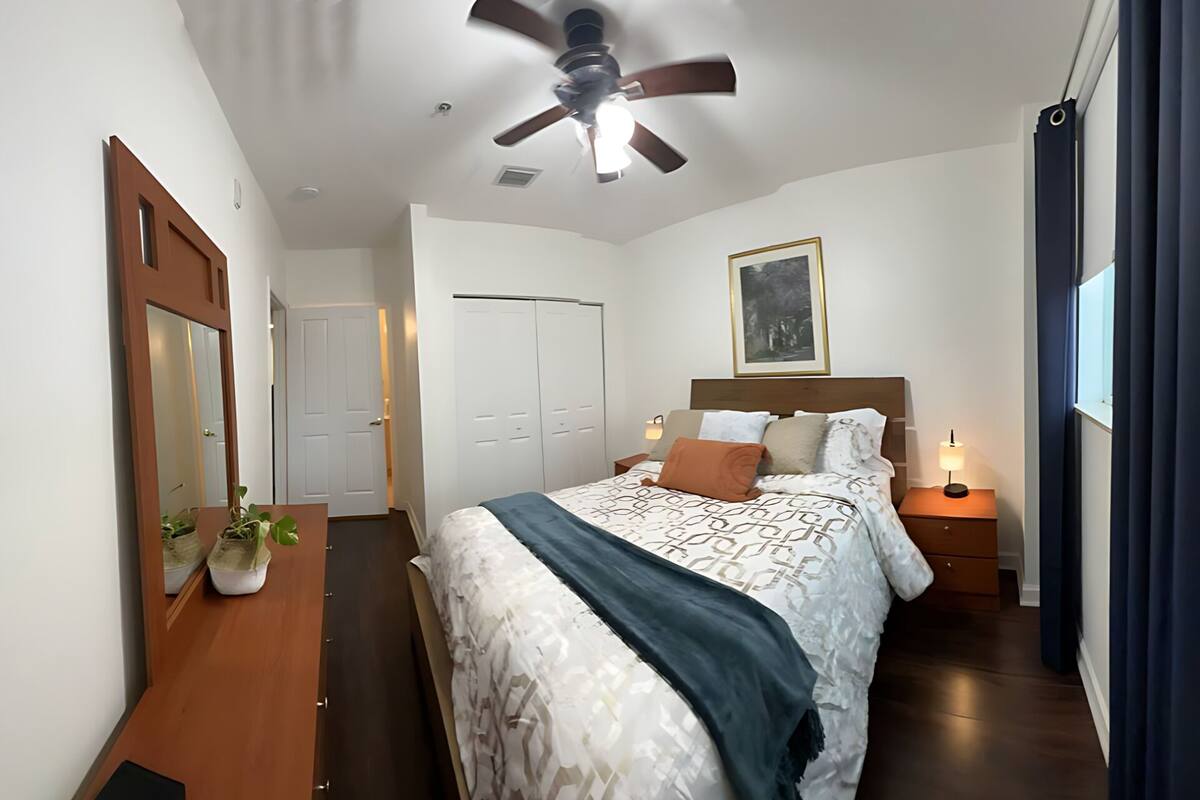 Une chambre à coucher avec un lit, des tables de chevet, un ventilateur de plafond, une porte et une fenêtre.