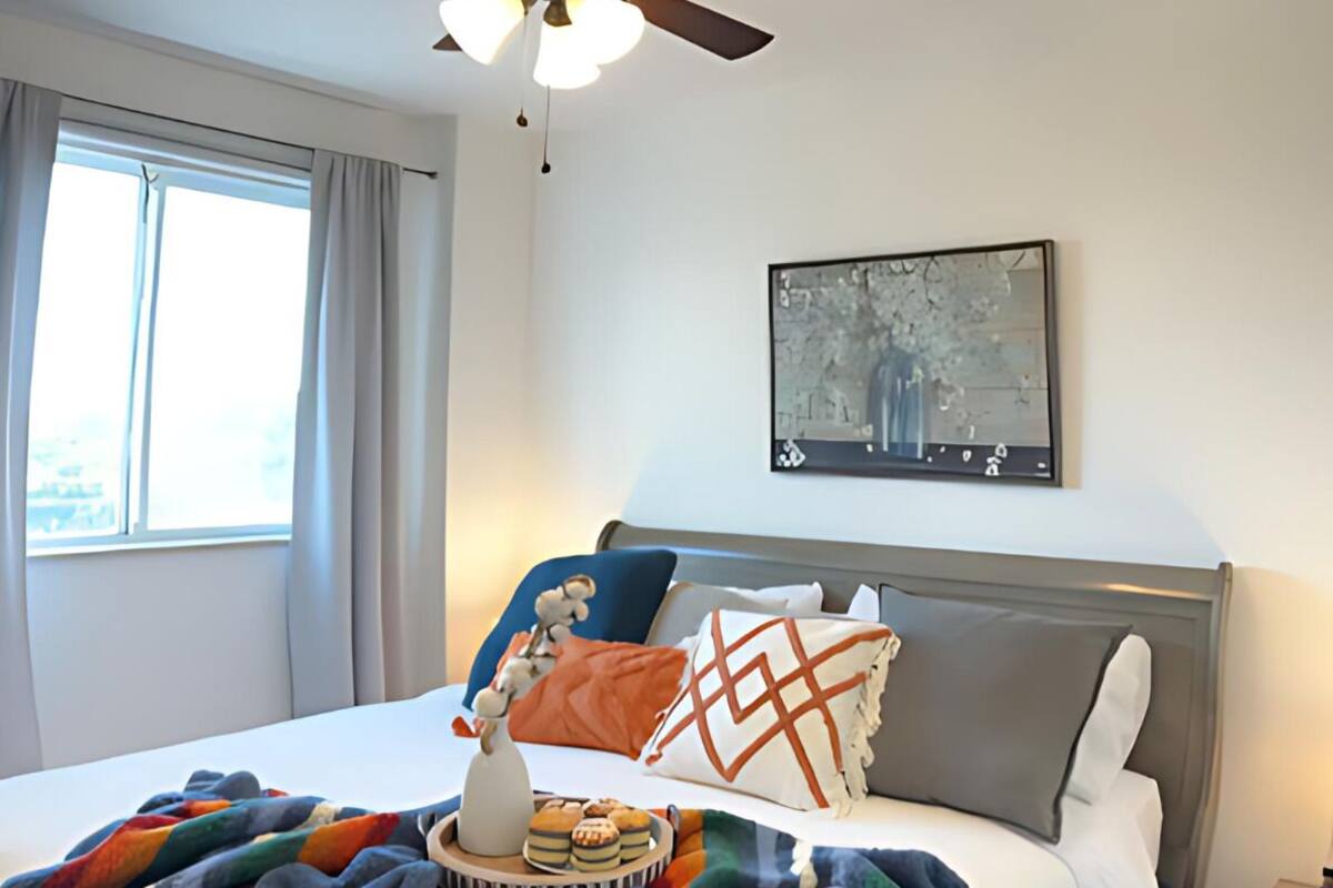 Une chambre à coucher avec un lit, un ventilateur de plafond, une fenêtre et un tableau accroché au mur.