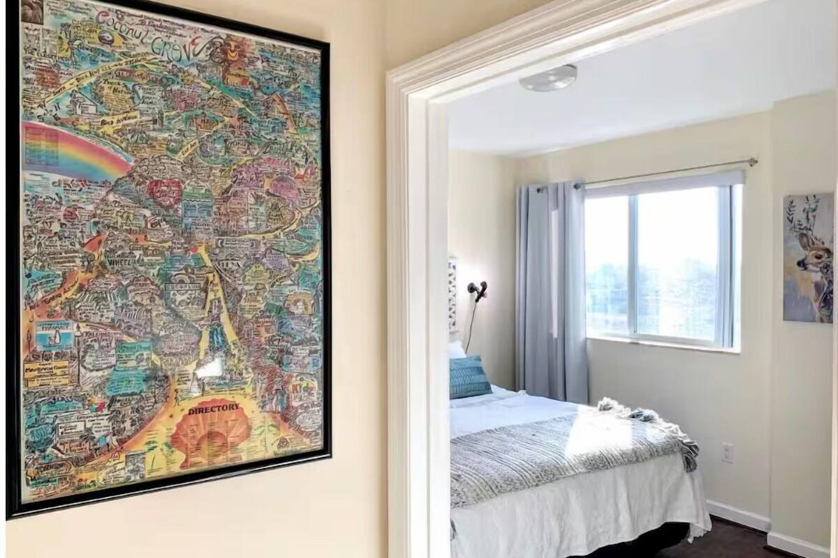 Une chambre à coucher avec un lit, une fenêtre avec des rideaux et une carte encadrée accrochée au mur.