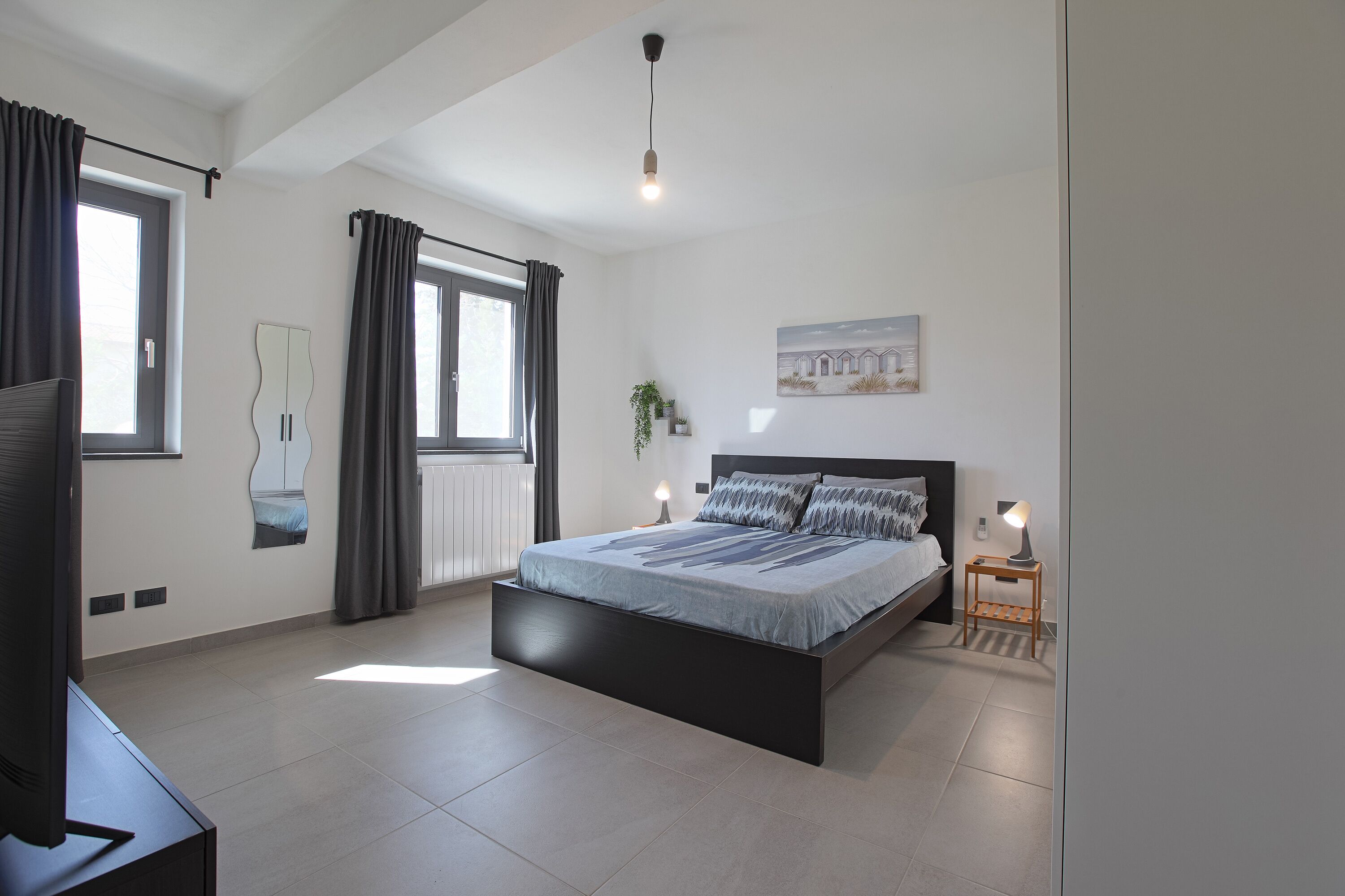 Un dormitorio moderno con una cama grande, un televisor y una pequeña mesa con lámpara.