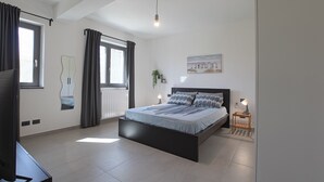 A modern bedroom with a large bed, a TV, and a small table with a lamp.
