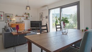 A modern living room with a dining table, sofa, TV, and artwork.