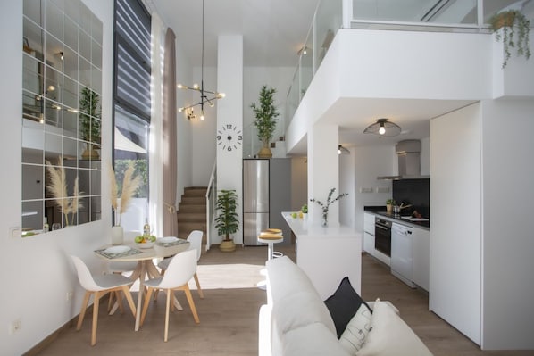 Une cuisine moderne avec des meubles blancs, un réfrigérateur en acier inoxydable et un coin repas comprenant une table et des chaises blanches.