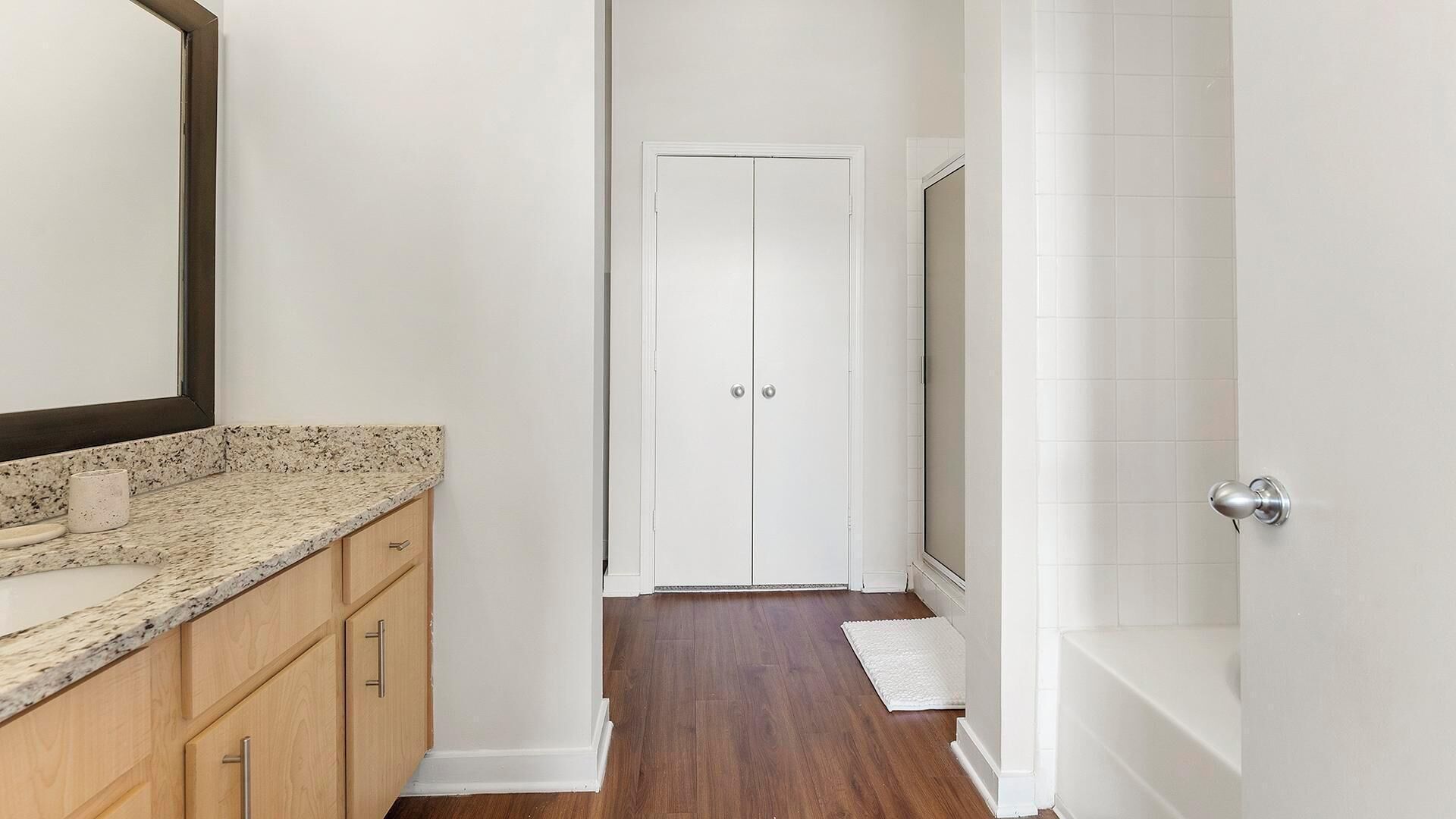 A narrow hallway with a wooden cabinet, a white door, and a white bathtub.