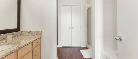A narrow hallway with a wooden cabinet, a white door, and a white bathtub.