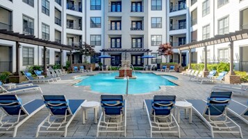 A rooftop pool with lounge chairs and umbrellas, surrounded by a multi-story building with balconies.