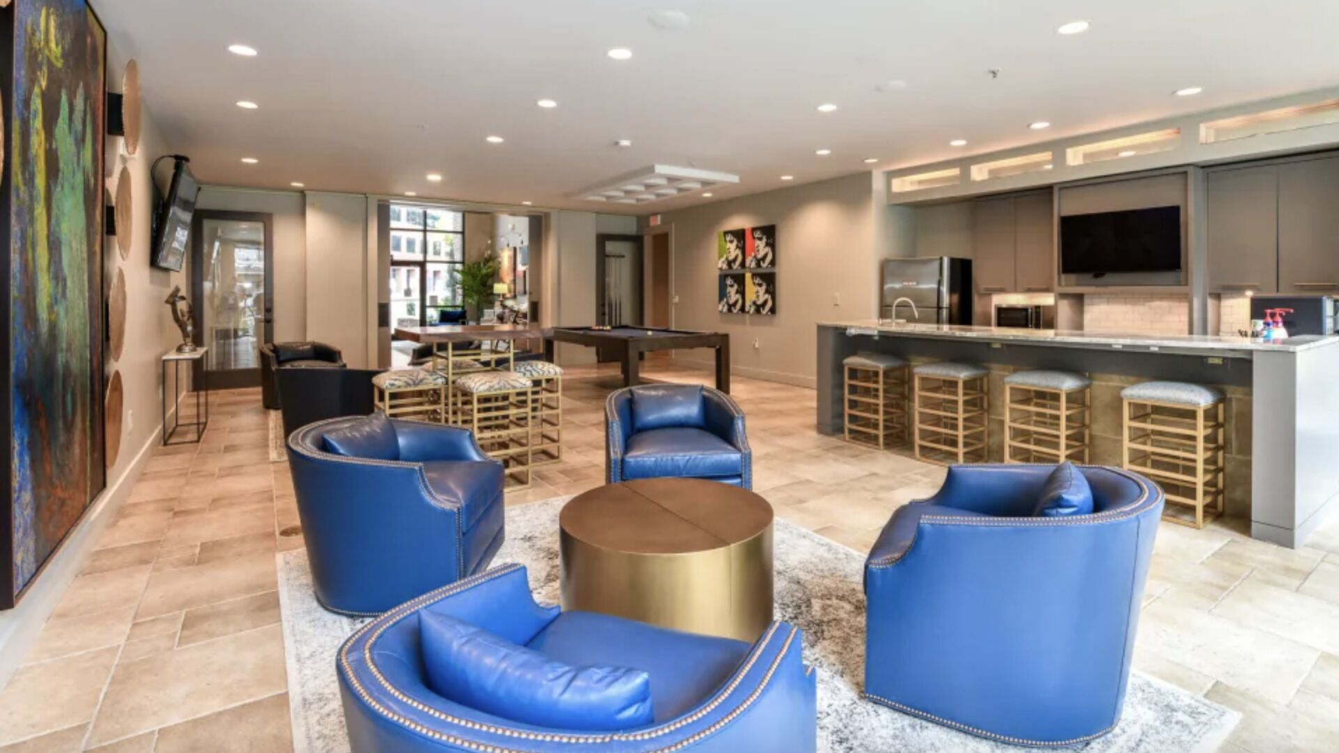 A spacious living area with blue leather sofas, a pool table, and a kitchen with bar stools.