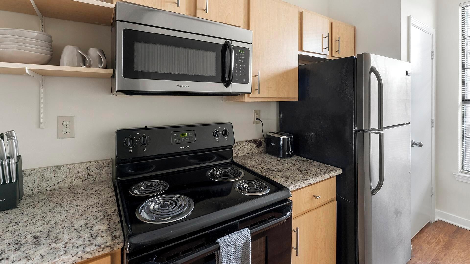 A kitchen with a stainless steel microwave, a black stove, and a black refrigerator.