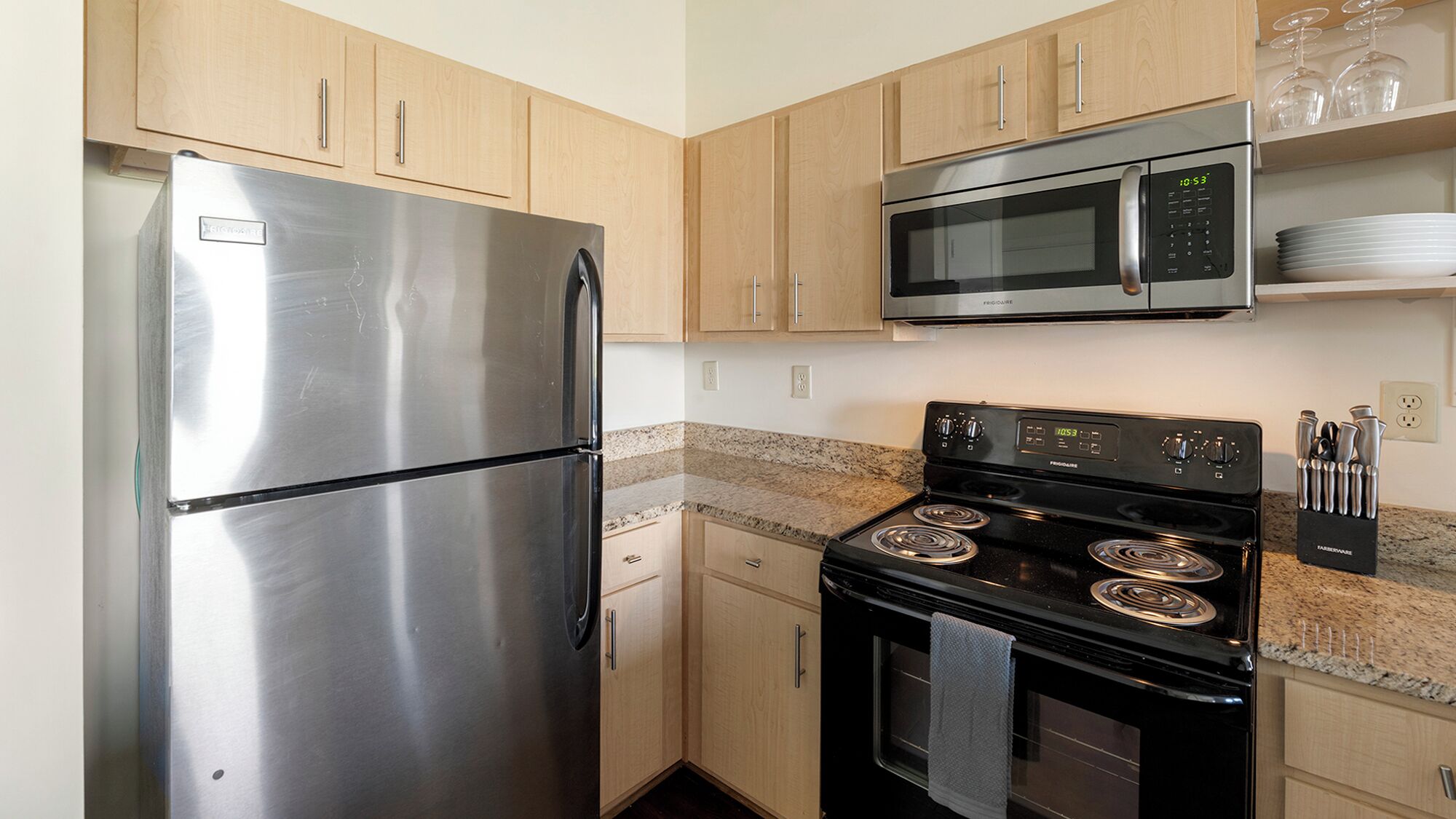 A compact kitchen with stainless steel appliances, wooden cabinets, and granite countertops.
