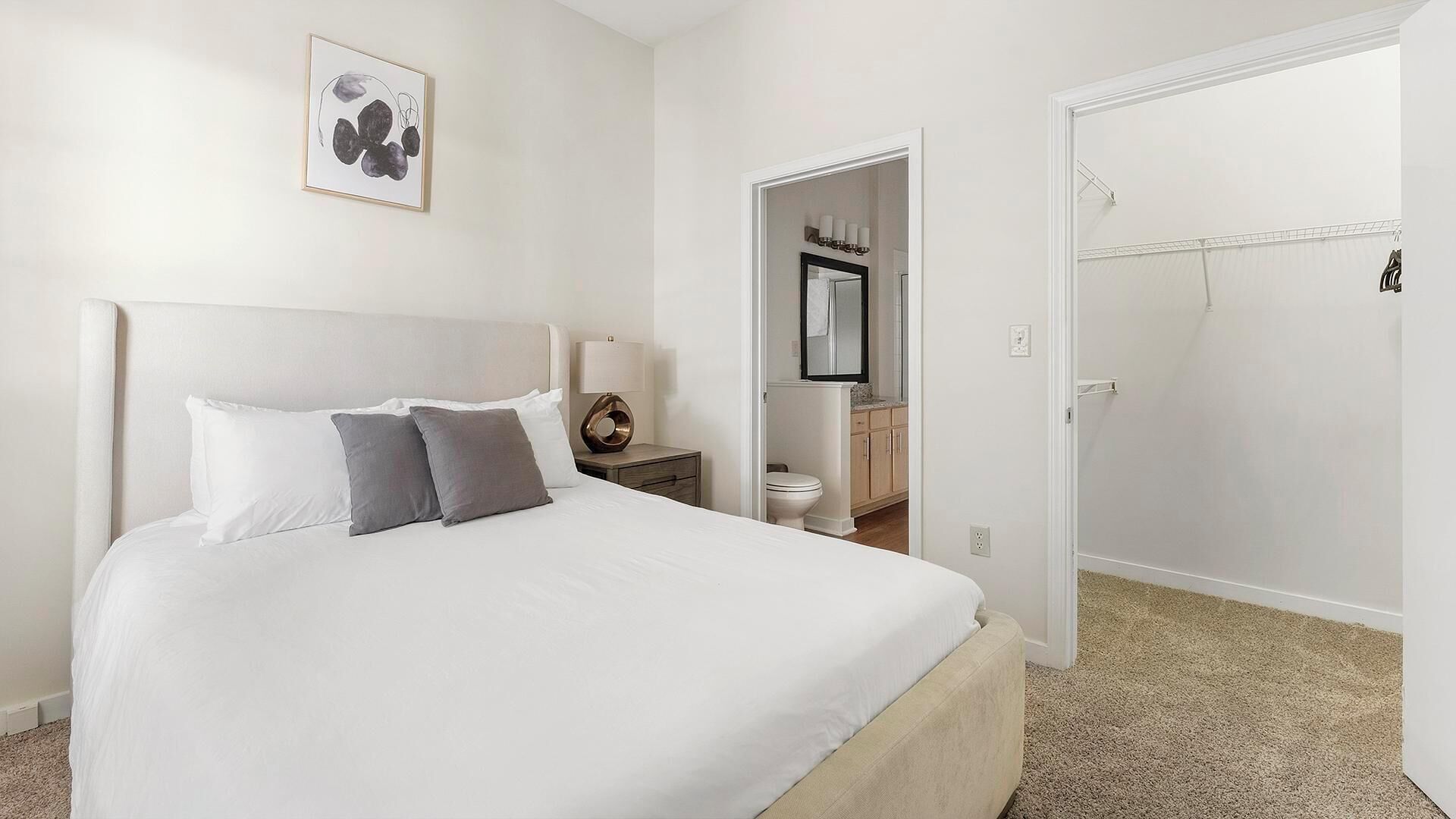 Un dormitorio con cama, mesita de noche, lámpara y un cuadro en la pared.
