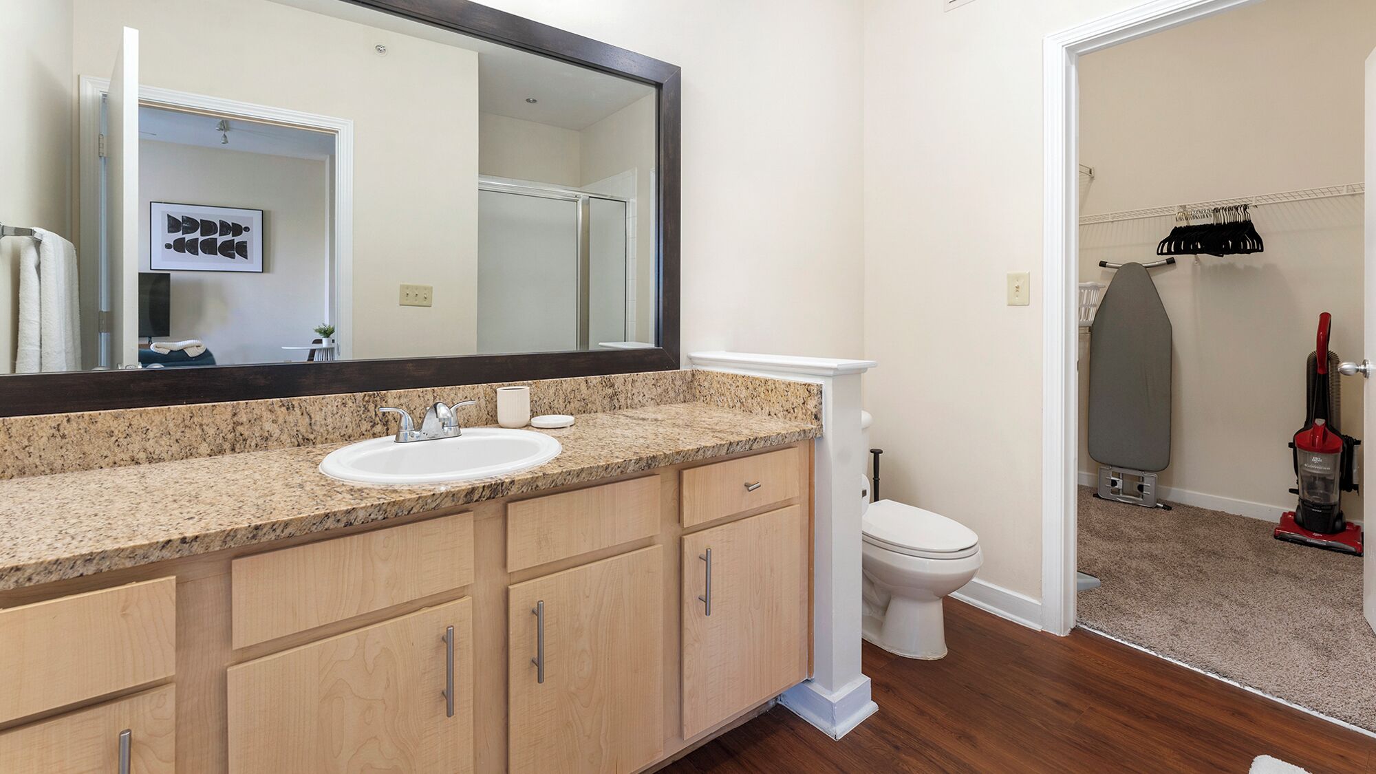 A bathroom with a granite countertop sink, a large mirror, and wooden cabinets.