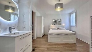 A bedroom with a white bed, a round mirror, a white dresser, and a wooden floor.