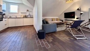 A modern loft apartment with a kitchen, living area, and a sloped ceiling.