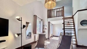 A modern living room with a flat-screen TV, two lounge chairs, a staircase, and a large window.