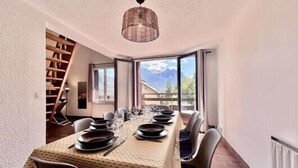 A dining area with a long table set for four, a staircase, and a view of mountains through large windows.