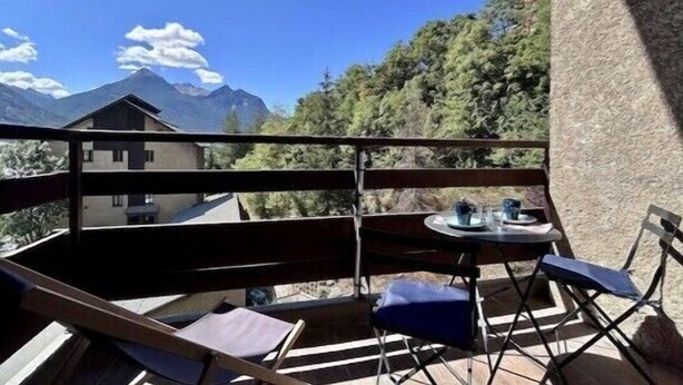 A balcony with a table and chairs, overlooking a mountain and trees.