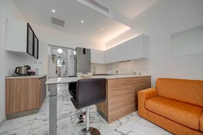 Una cocina moderna con piso de mármol, gabinetes de madera, un taburete negro y un sofá naranja.
