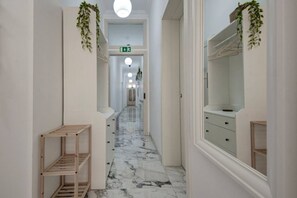 Un pasillo con piso de mármol, estantes de madera, un espejo y plantas colgantes.