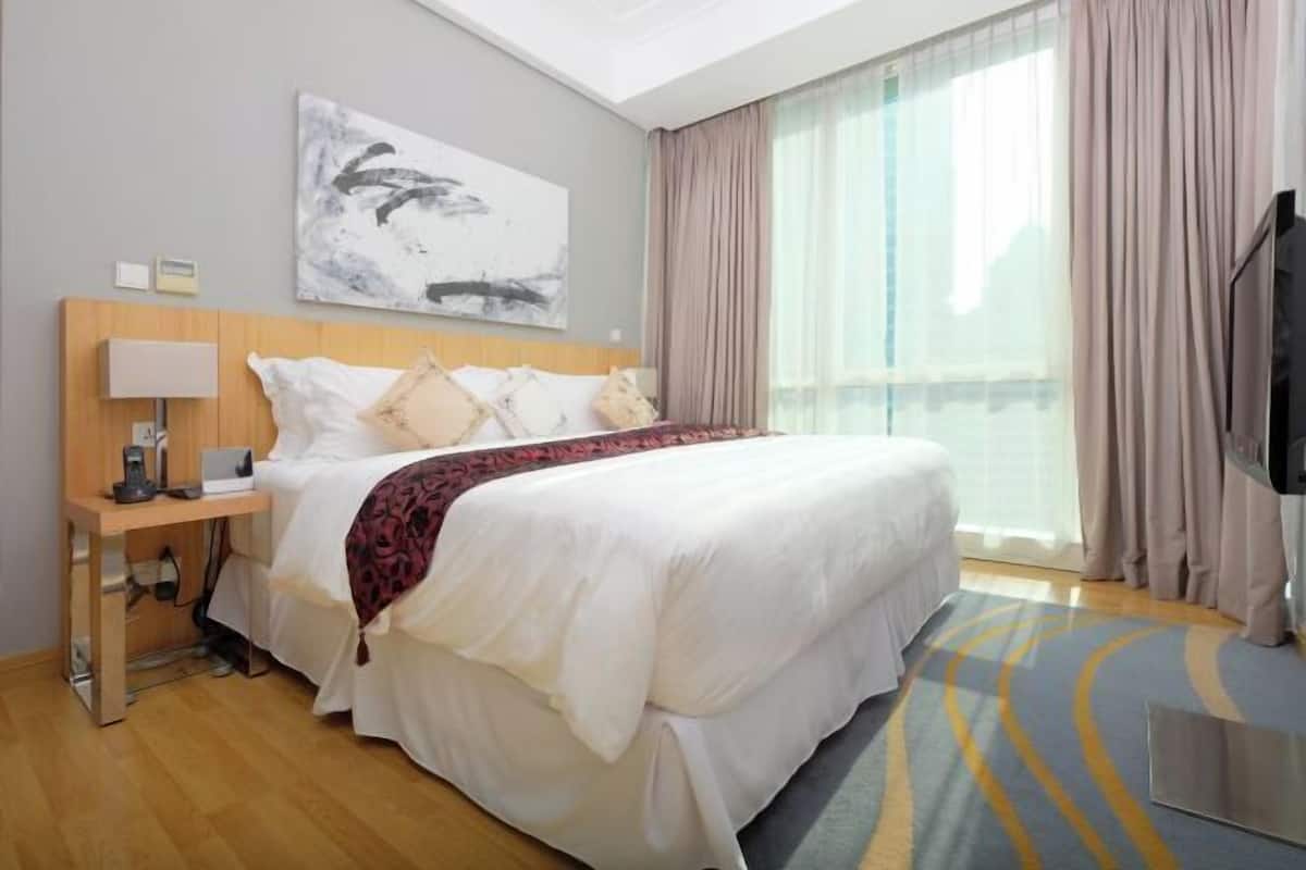 Une chambre d’hôtel avec un lit, une table de chevet avec une lampe, une télévision et une grande fenêtre avec des rideaux.