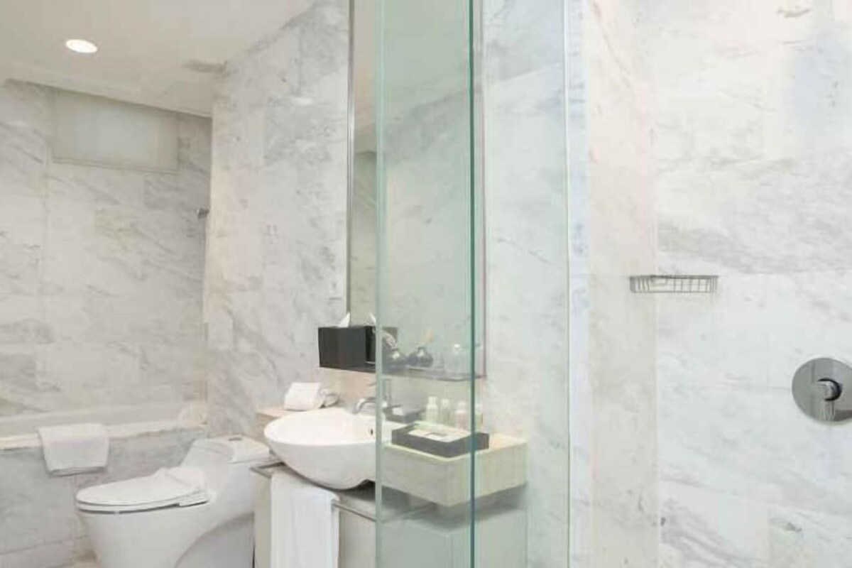 Une salle de bain moderne avec une douche à parois de verre, des toilettes blanches et un lavabo doté d’un plan de travail en marbre.