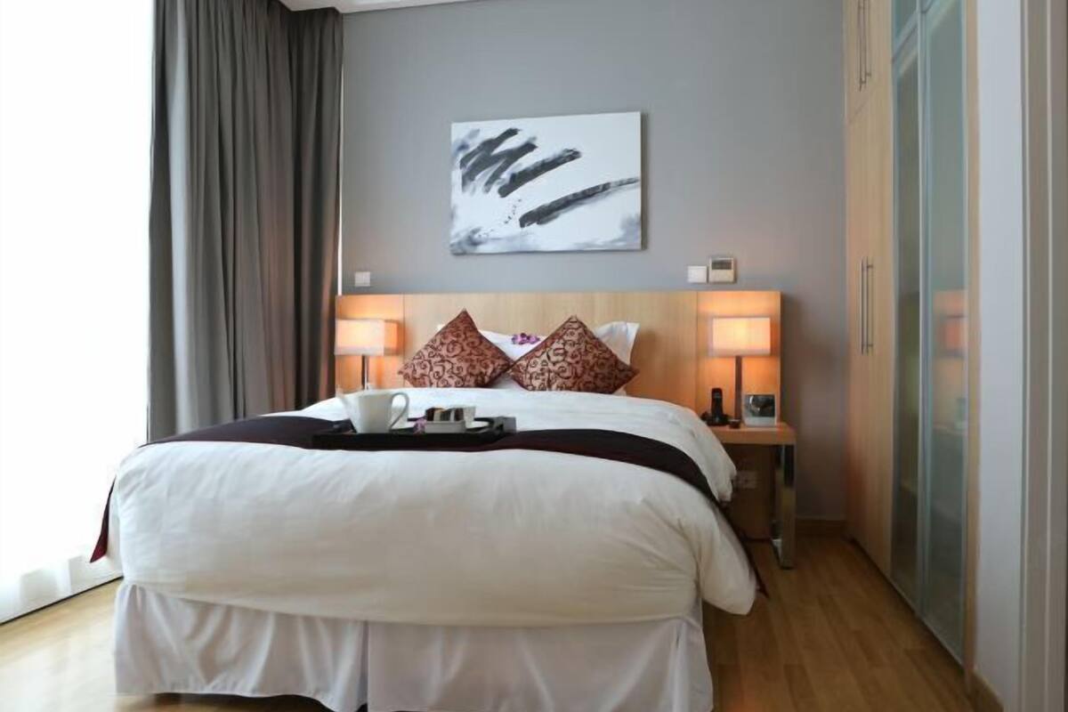Une chambre d’hôtel avec un grand lit, deux lampes de chevet, un tableau au mur et une vue sur l’extérieur.