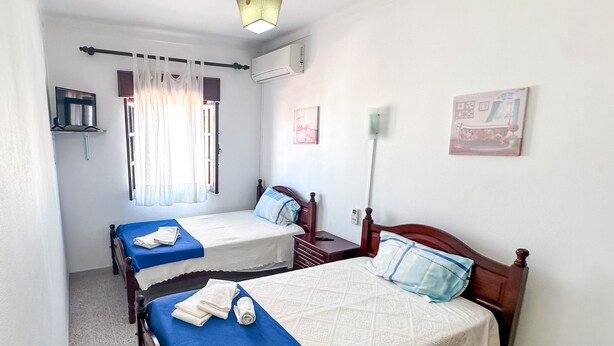 A hotel room with two single beds, a TV, an air conditioning unit, and a window with curtains. - Residencial Boavistense by Umbral (Odemira)