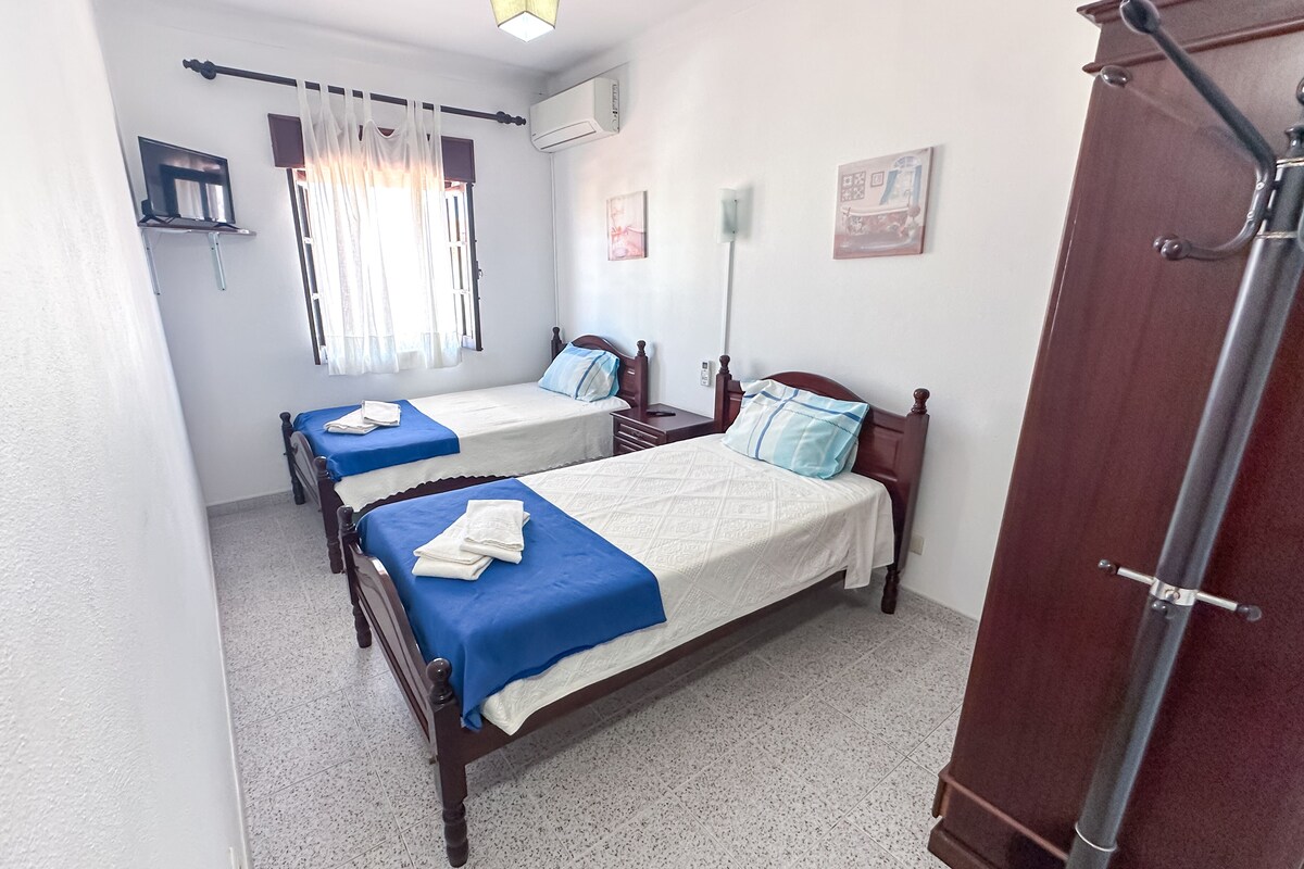 Una habitación con dos camas de madera, cada una con colcha azul y blanca, y un armario de madera.