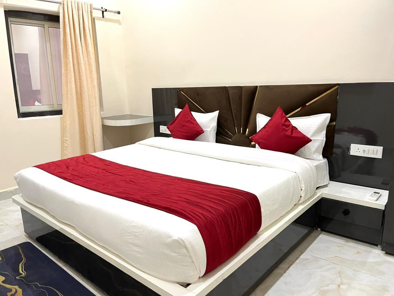 Ein modernes Hotelzimmer mit einem großen Bett, roter und weißer Bettwäsche, einem dunklen Kopfteil und einem Nachttisch mit einem Telefon.