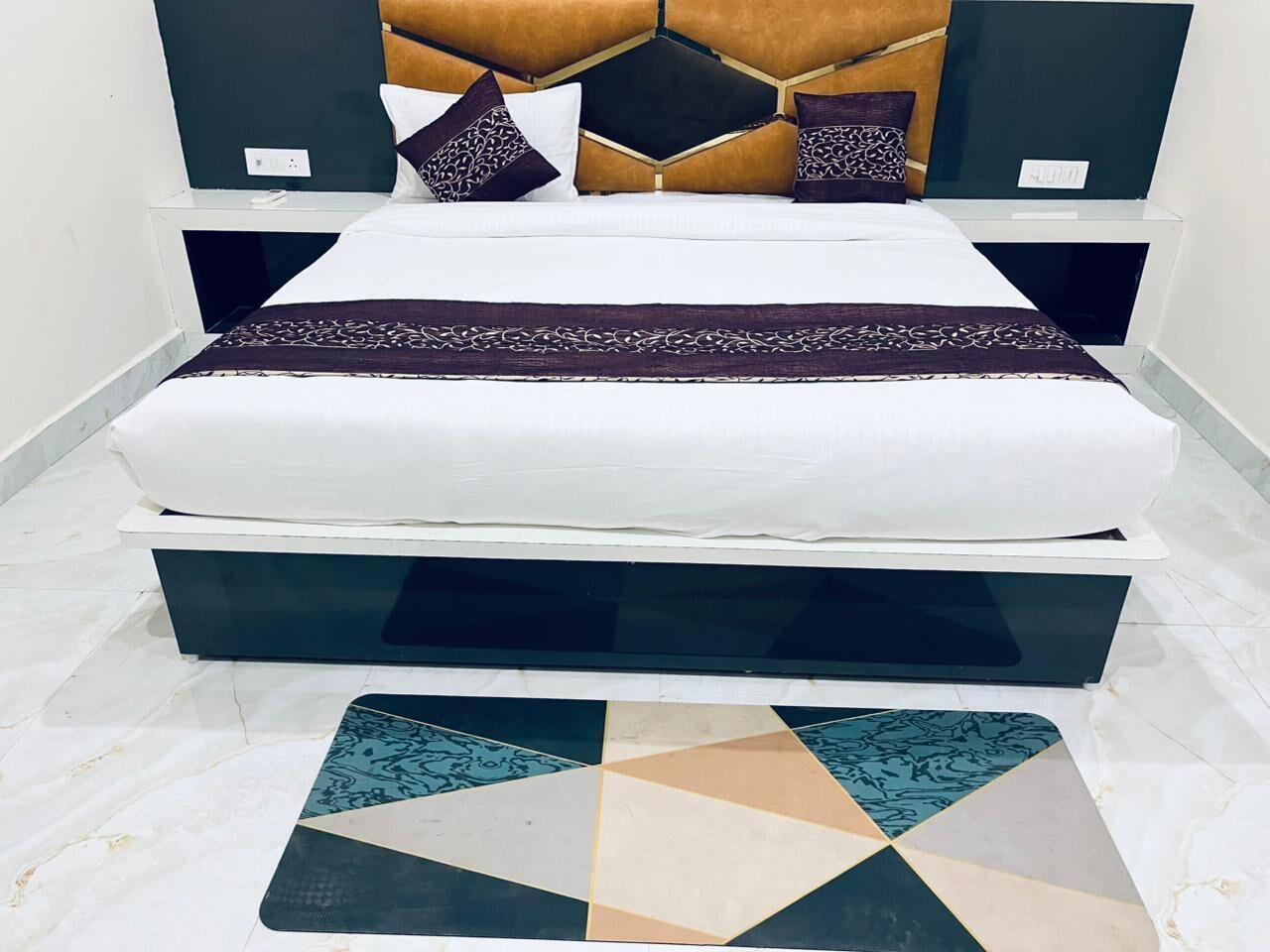 A bed with a white mattress, a geometric-patterned rug, and a headboard with a geometric design.