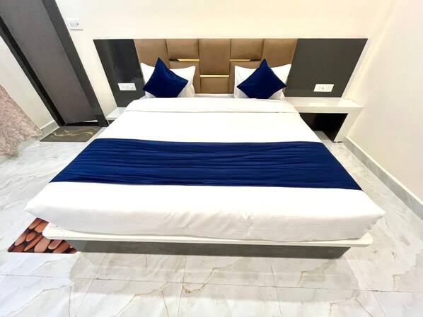 A bed with a white mattress and blue bedding, a headboard with a light wood finish, and a marble floor. - Hotel Basant Orchha (Nivari)