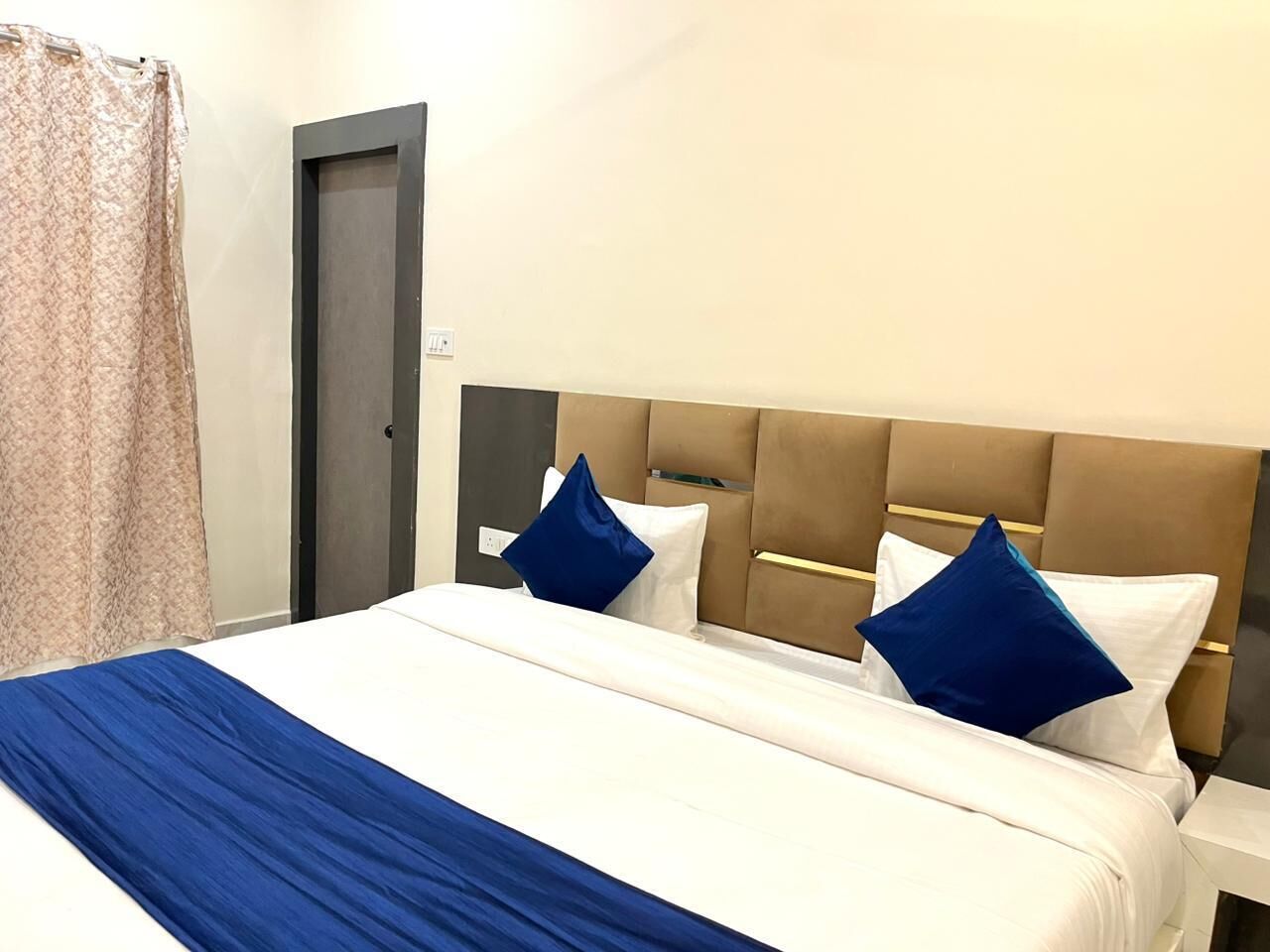 A hotel room with a large bed, two pillows, a headboard, and a door.