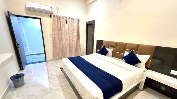 Una camera d'albergo con un letto grande, un comodino, una testiera, una tenda e una vista attraverso una porta.