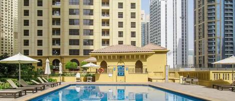 A swimming pool with lounge chairs and umbrellas, surrounded by high-rise buildings.