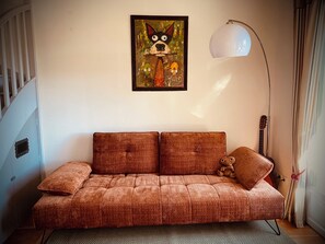 Un canapé avec un coussin, une lampe, une guitare et un tableau accroché au mur.